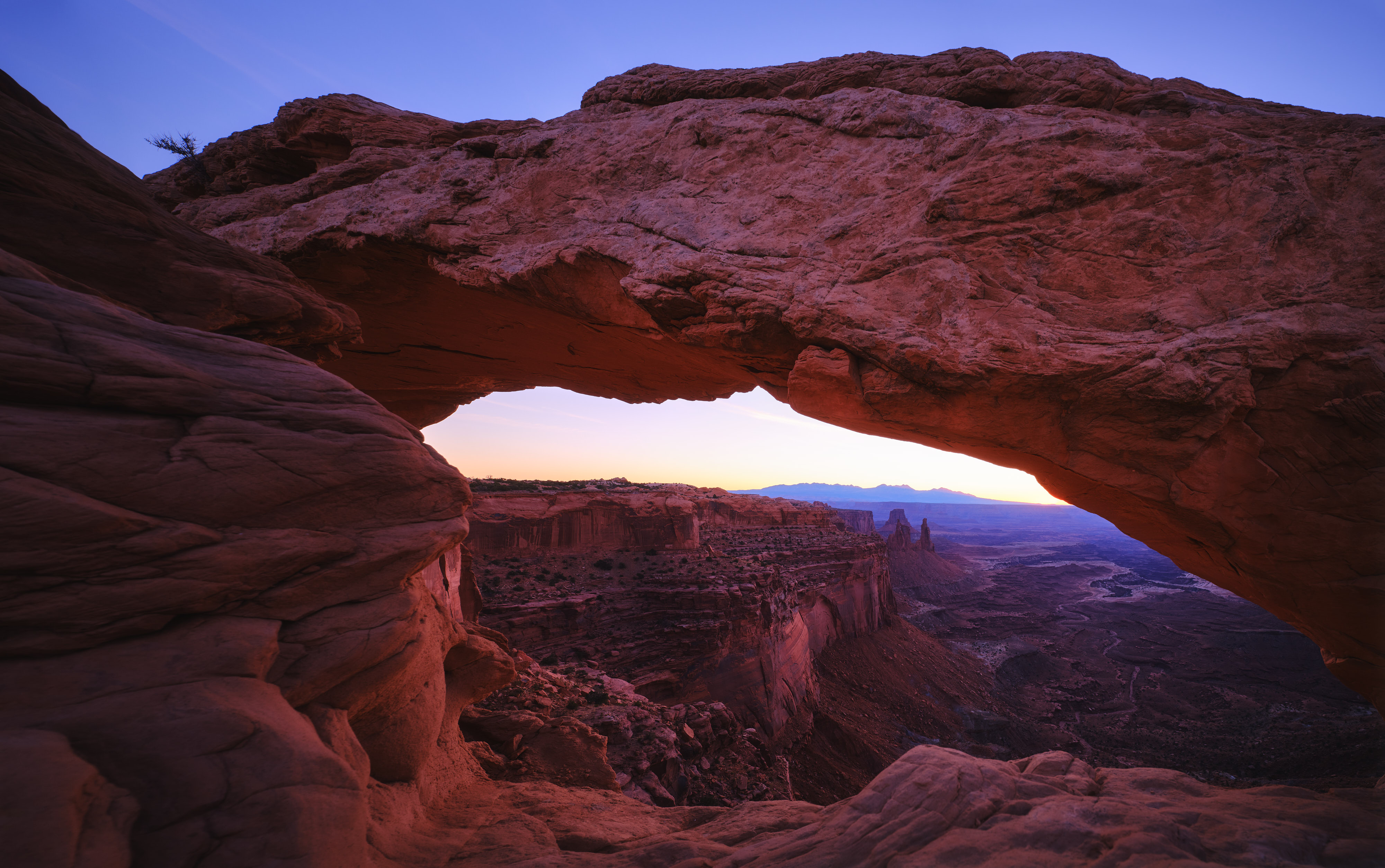 Dawn at Mesa Arch with a soft orange hue over the La Salle Mountain Range.